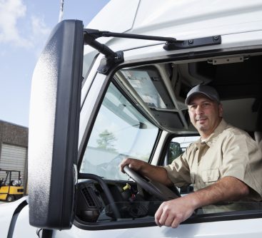 Truck driver (30s) sitting in cab of semi-truck.